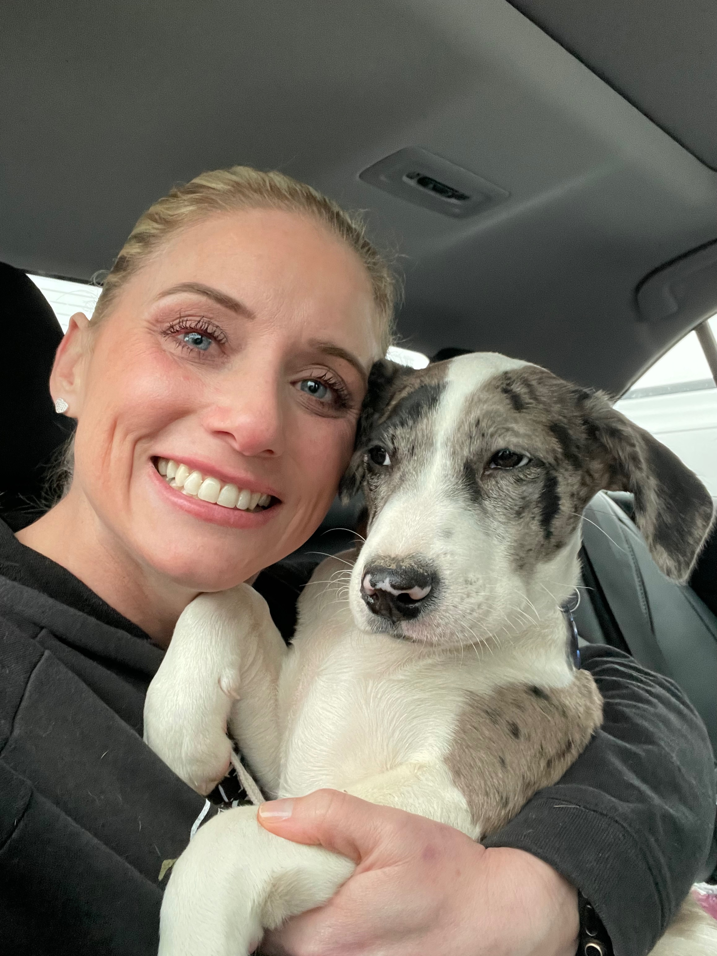 A smiling woman holding a gray-and-white puppy inside a vehicle