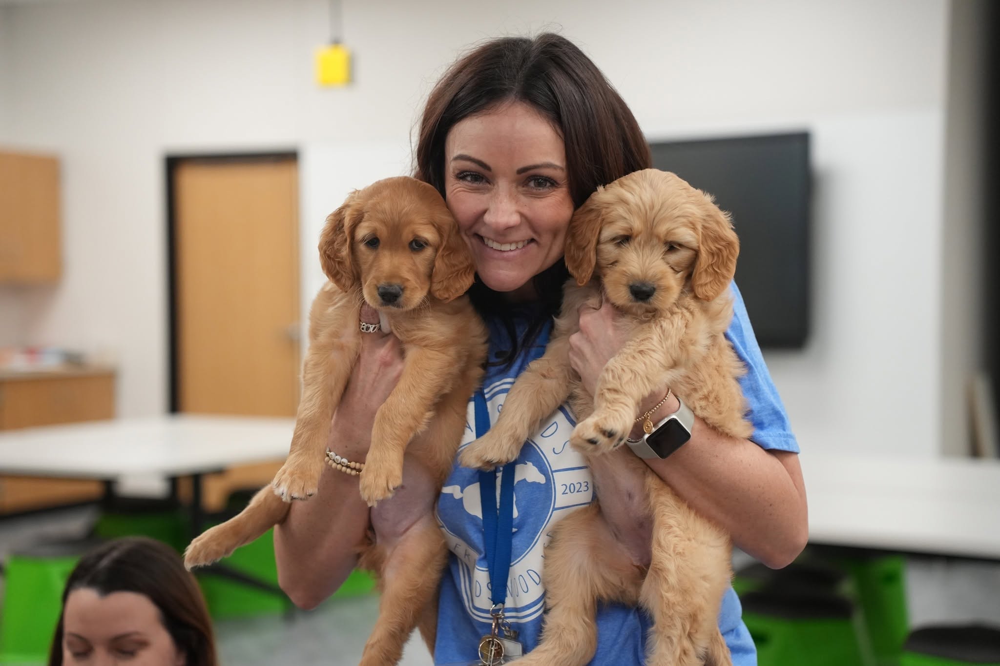 A smiling woman holding two puppies in a rescue care room