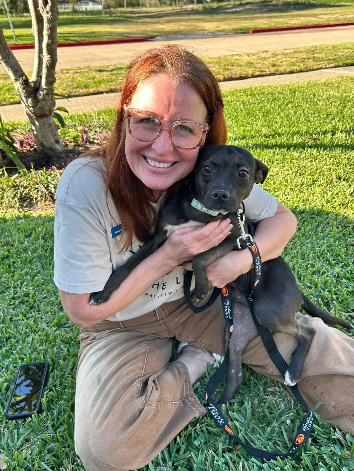 A woman sitting outdoors and cuddling a brindle dog