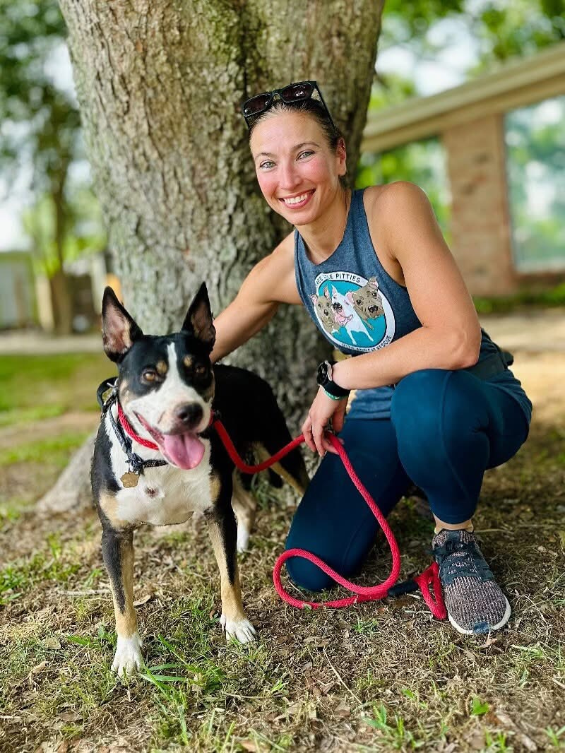 A woman crouching beside a black-and-white dog beneath a tree
